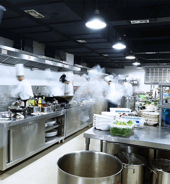A busy kitchen with chefs in white uniforms working on various dishes, surrounded by cooking equipment and ingredients. Steam rises from pots and pans as they prepare meals.