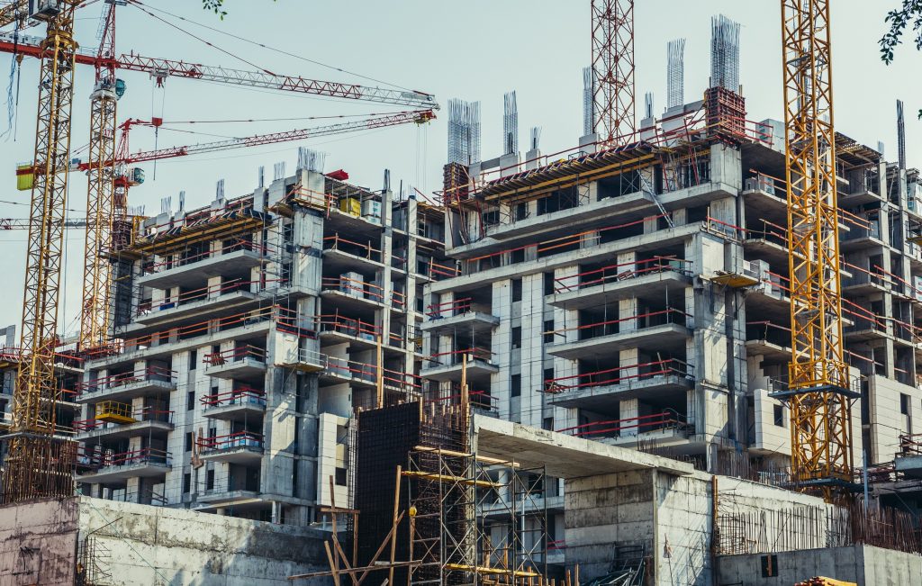 A construction site featuring multiple unfinished buildings with cranes and scaffolding. The structures are in various stages of development.
